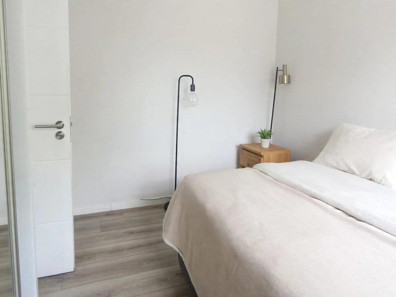 A bright and neutral bedroom featuring modern laminate flooring and a built-in wardrobe.
