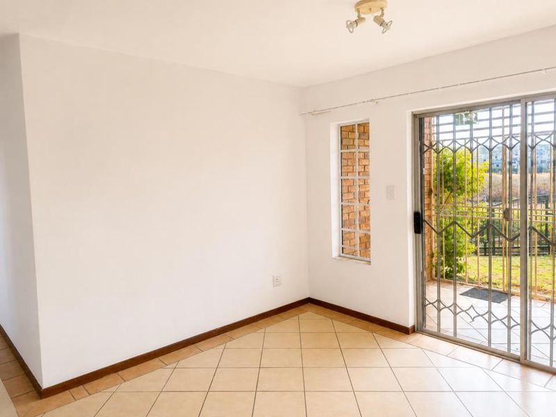 An empty living area featuring ceramic floor tiles, a brick feature window, and a sliding glass door with security gate leading to the exterior.