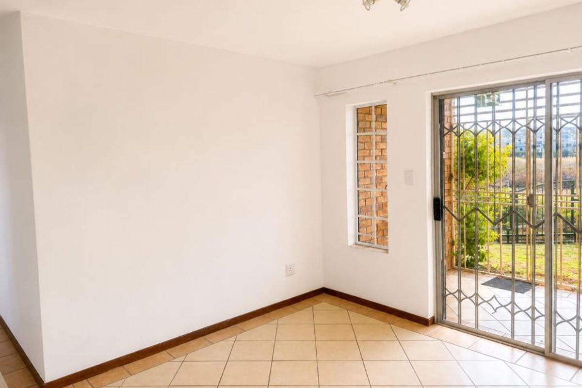 An empty living area featuring ceramic floor tiles, a brick feature window, and a sliding glass door with security gate leading to the exterior.