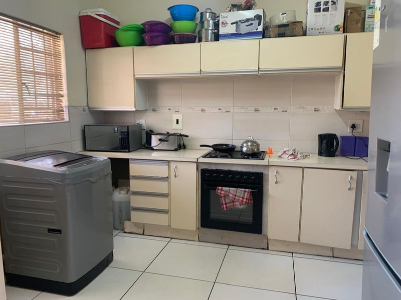 A functional kitchen featuring built-in cabinetry, a hob, an oven, and tiled flooring, offering a practical layout with potential for cosmetic updates.