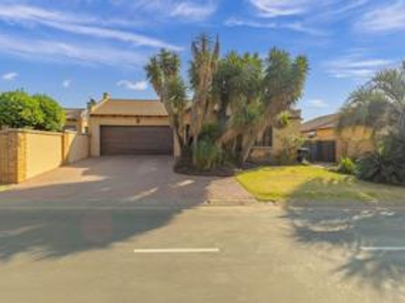 Front elevation of a cluster home featuring a paved driveway, double garage, and established garden with boundary walling.