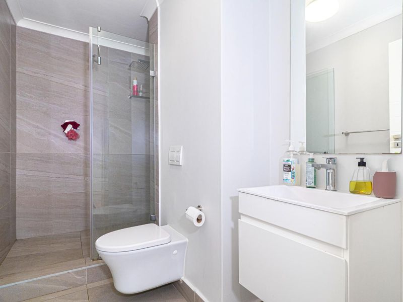 Modern bathroom featuring a wall-mounted toilet, glass-enclosed shower with rain head, and a sleek vanity with basin.