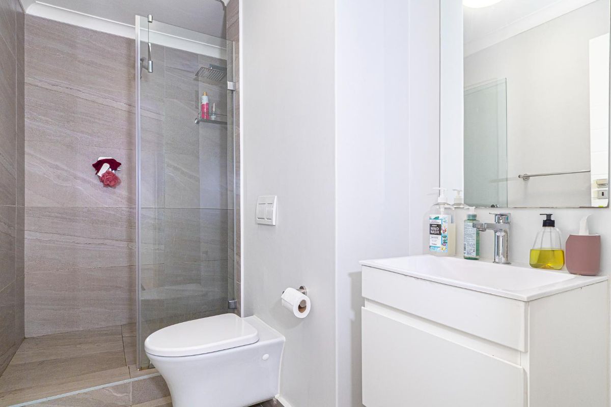Modern bathroom featuring a wall-mounted toilet, glass-enclosed shower with rain head, and a sleek vanity with basin.