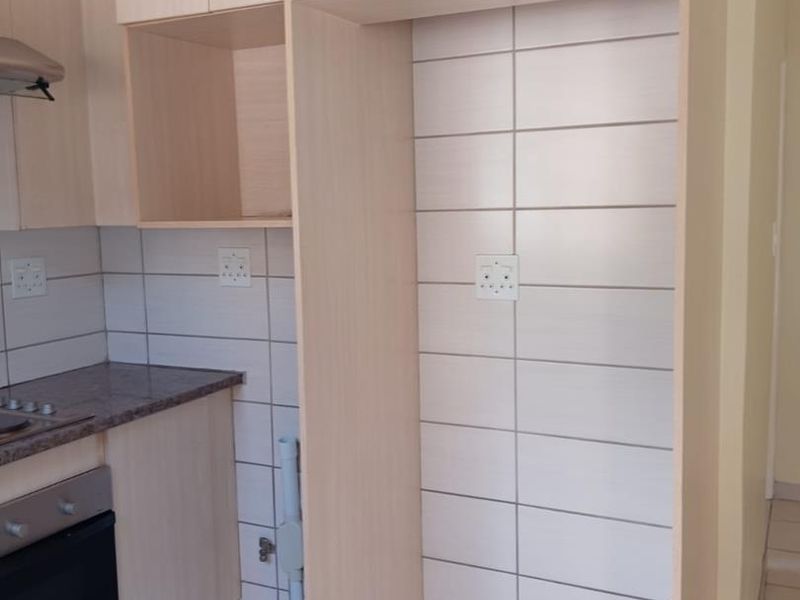A clean, functional kitchen featuring light wood-tone cabinetry, tiled backsplash, built-in oven, hob, and a dedicated alcove for a refrigerator.