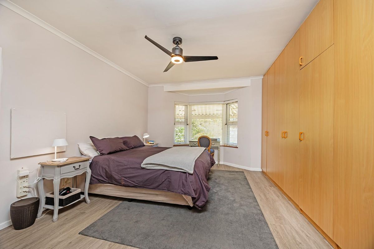 A well-lit bedroom featuring built-in wooden wardrobes, a ceiling fan, and a bay window that allows for natural light.