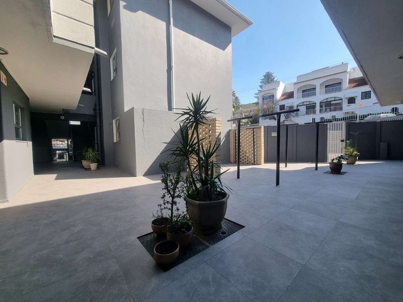 A paved communal courtyard area featuring a brick privacy screen, metal washing line infrastructure, and modern grey floor tiling.