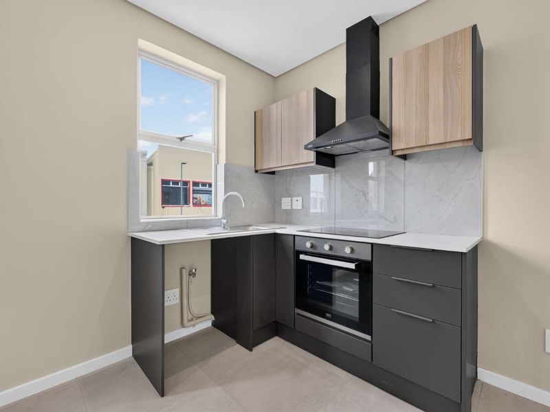 Modern kitchen featuring sleek dark grey cabinetry, light wood-tone upper cabinets, stone countertops, integrated oven, hob, and extractor fan with marble-look splashback.