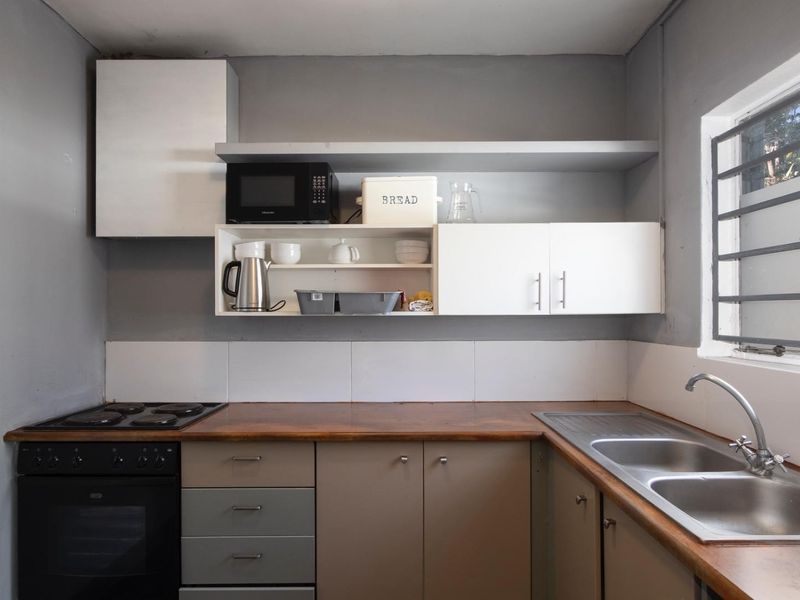 Compact kitchen featuring wooden countertops, double basin sink, built-in oven with electric hob, and ample wall-mounted cabinetry with a tiled splashback.