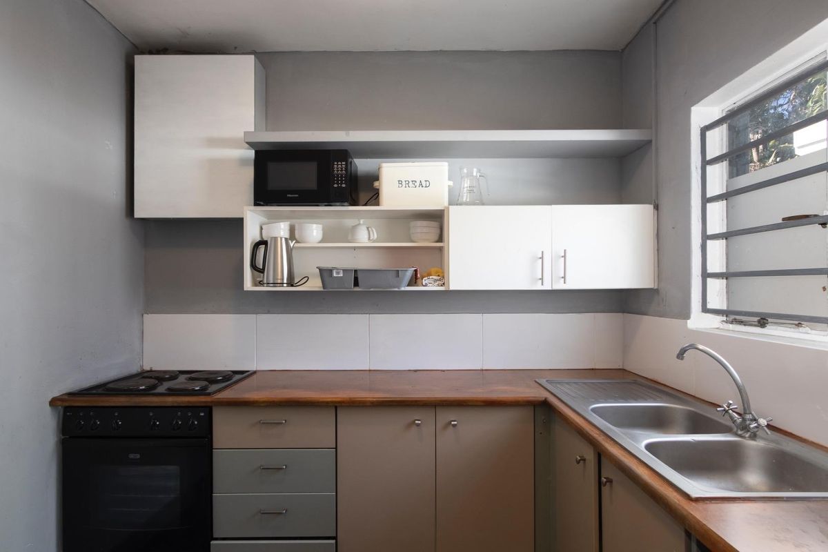 Compact kitchen featuring wooden countertops, double basin sink, built-in oven with electric hob, and ample wall-mounted cabinetry with a tiled splashback.