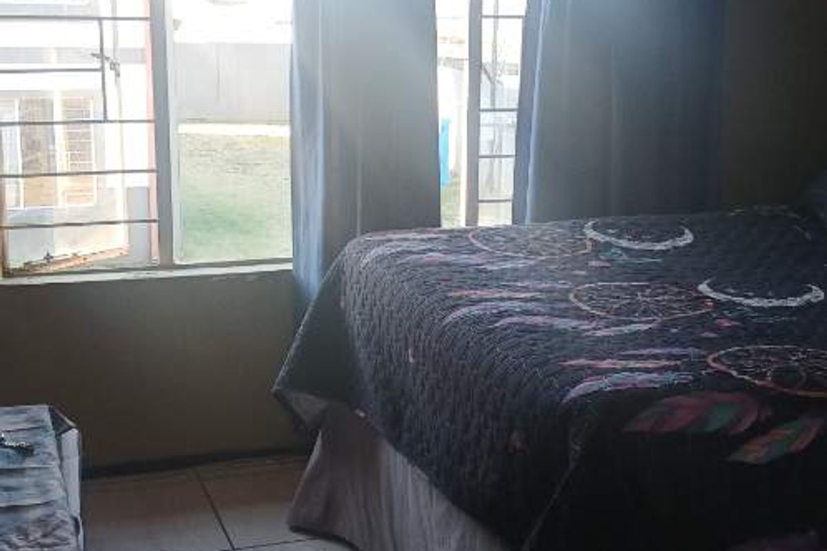 A bedroom featuring tiled flooring and windows fitted with security bars, allowing natural light into the space.