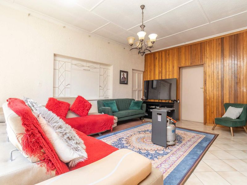 A living room featuring wood paneling, tiled flooring, and a central chandelier, offering a dated but functional space with potential for modernization.