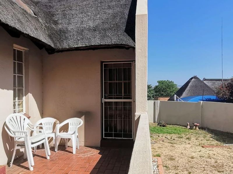 A covered patio area featuring brick paving, a thatch roof overhang, and a security gate, overlooking a small private garden space.