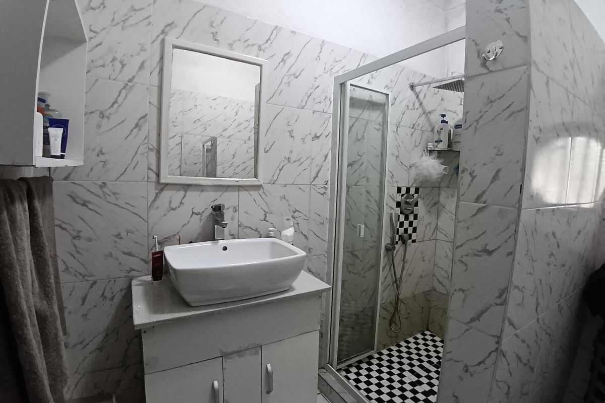 A functional bathroom featuring a vessel sink vanity, a glass-enclosed shower with a rainfall showerhead, and marble-effect wall tiling.