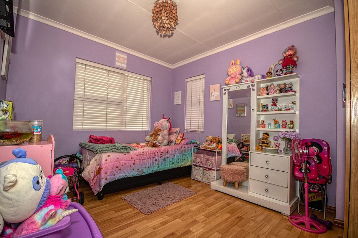 A bedroom featuring laminate flooring, purple painted walls, and white venetian blinds.