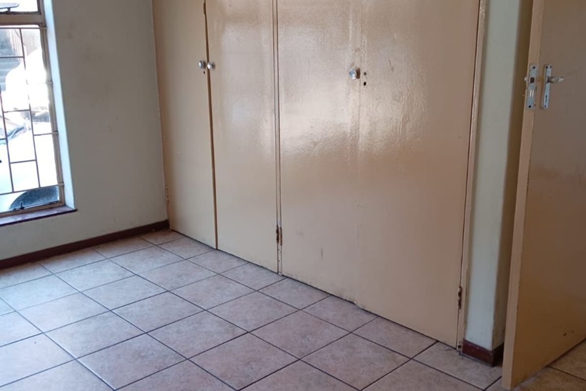 An empty bedroom featuring tiled flooring and extensive built-in cupboards with security bars on the window.