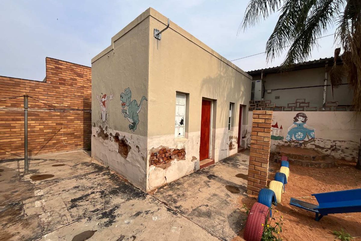 Exterior view of a small outbuilding featuring weathered plaster, exposed brickwork, and a paved yard area.
