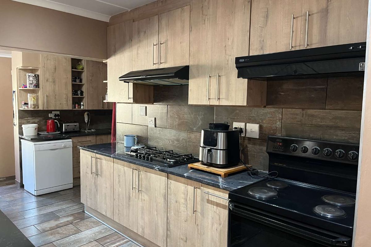 A functional kitchen featuring wood-look cabinetry, dark stone-effect countertops, tiled backsplash, a gas hob, and a built-in oven with an extractor fan.