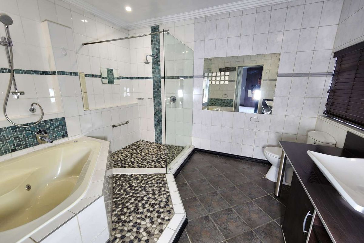 Spacious bathroom featuring a walk-in shower with pebble flooring, a built-in bathtub, and a modern vanity with a vessel sink.