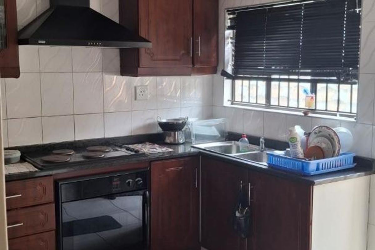 A functional kitchen featuring dark wood cabinetry, a built-in oven with extractor fan, double sink, and tiled flooring throughout.