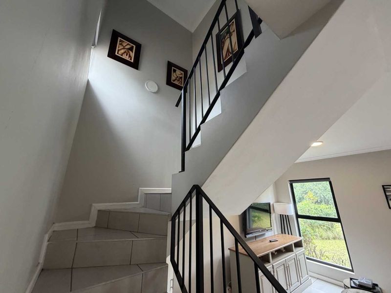 A bright hallway featuring a staircase with a modern metal balustrade and tiled steps, leading to the upper level of the townhouse.