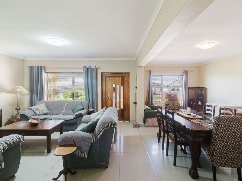 Spacious open-plan living and dining area featuring neutral tiled flooring, natural light through large windows, and a solid wooden front entrance door.