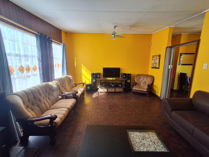 A spacious living room featuring traditional parquet flooring, a ceiling fan, and bright yellow walls, offering a functional layout with natural light.