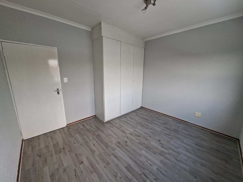 A clean, empty bedroom featuring grey laminate flooring, neutral walls, and a built-in wardrobe, providing a versatile space ready for personalization.