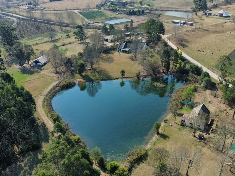 Aerial view of a sprawling farm property featuring a large private dam, multiple outbuildings, and extensive open grazing land.