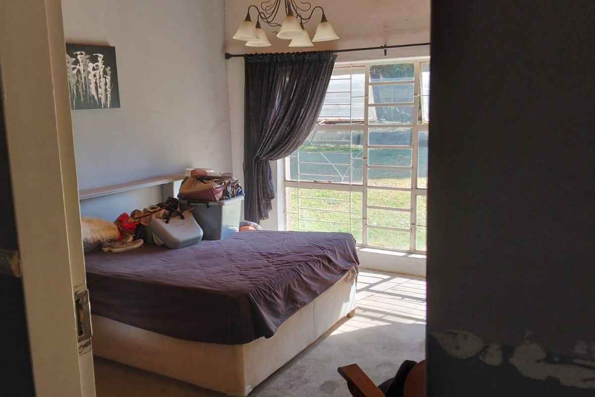 A bedroom featuring a large window with a visible crack in the glass, providing natural light and a view of the garden.