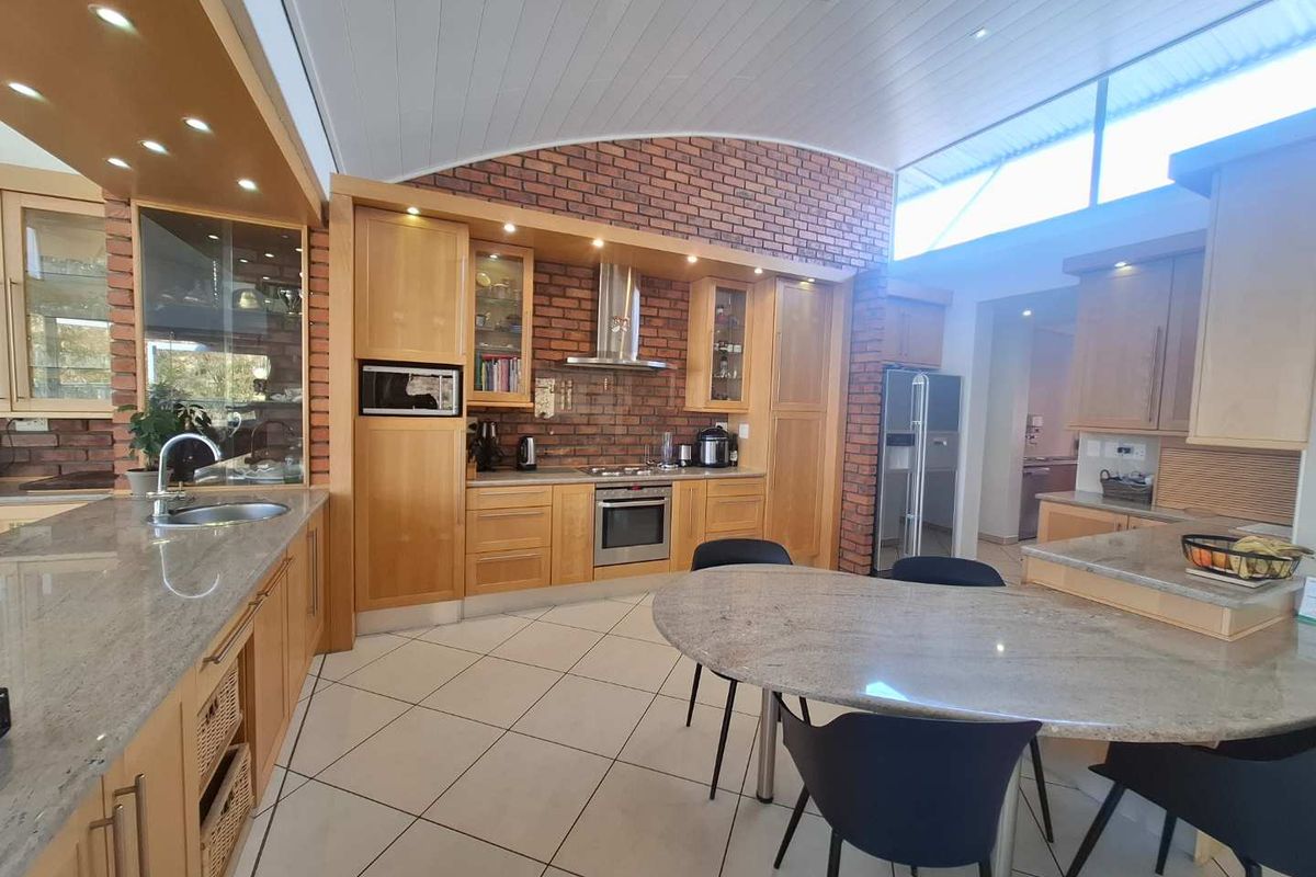 Spacious kitchen featuring light wood cabinetry, granite countertops, a central island, and a distinctive exposed brick feature wall under a vaulted ceiling.