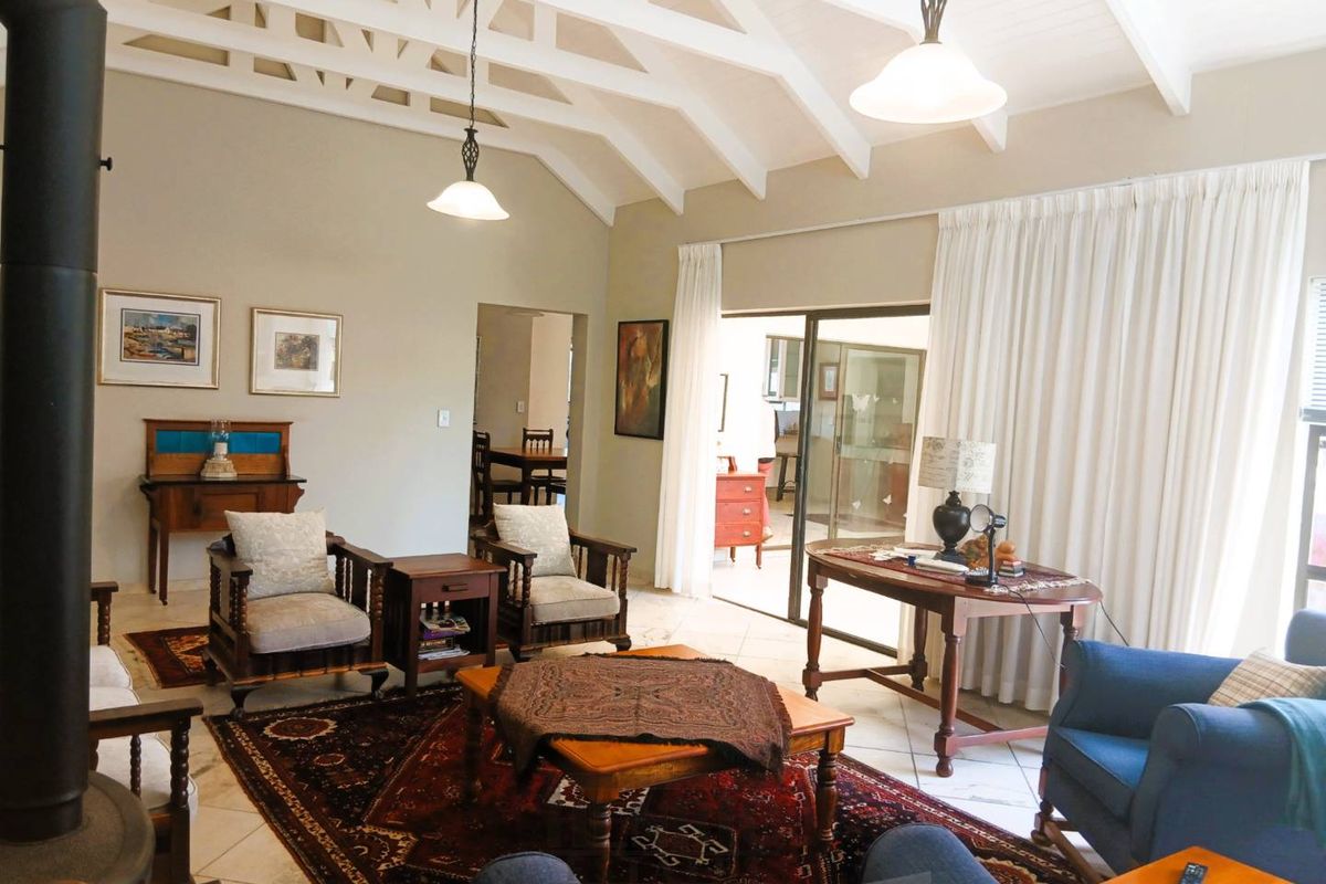 Spacious living room featuring a high vaulted ceiling with exposed rafters, tiled flooring, and a freestanding fireplace, with direct access to an outdoor area.