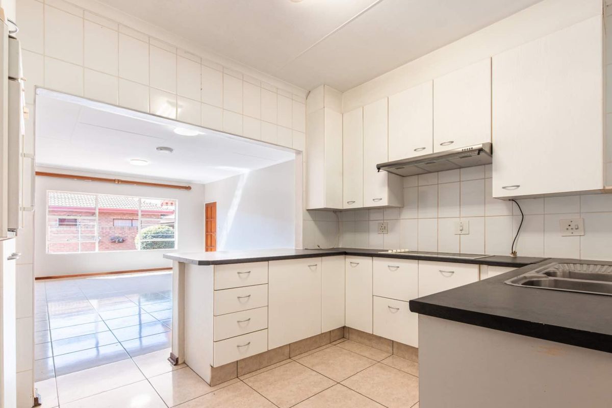 A functional kitchen featuring white cabinetry, dark countertops, and a built-in extractor fan, with an open-plan layout connecting to the adjacent living area.