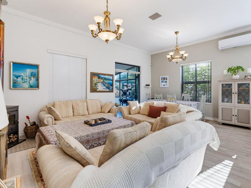 Spacious open-plan living and dining area featuring a wood-burning stove, split-system air conditioning, and elegant chandeliers with neutral flooring.
