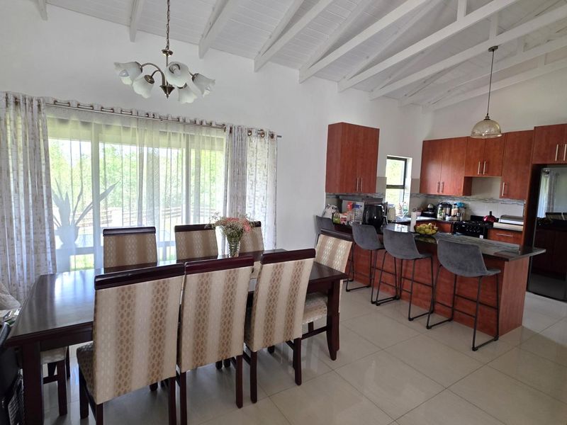 Spacious open-plan kitchen and dining area featuring high exposed beam ceilings, modern cabinetry, a functional kitchen island, and large windows for natural light.
