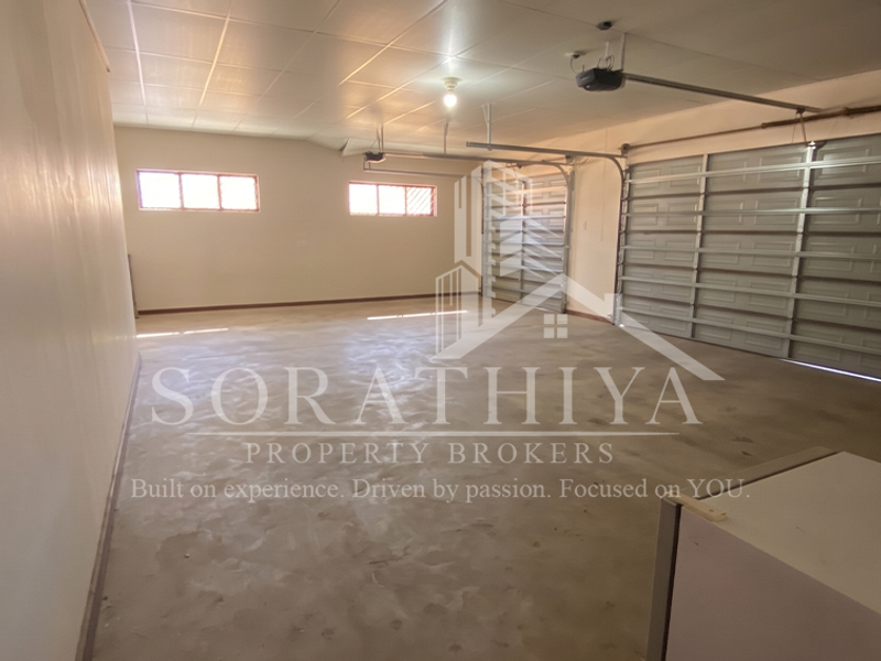 A spacious, empty double garage featuring concrete flooring, a tiled ceiling, and automated garage door mechanisms.