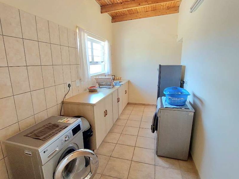 Functional laundry room featuring tiled flooring, built-in cabinetry with a tiled splashback, and a distinctive timber beam ceiling.