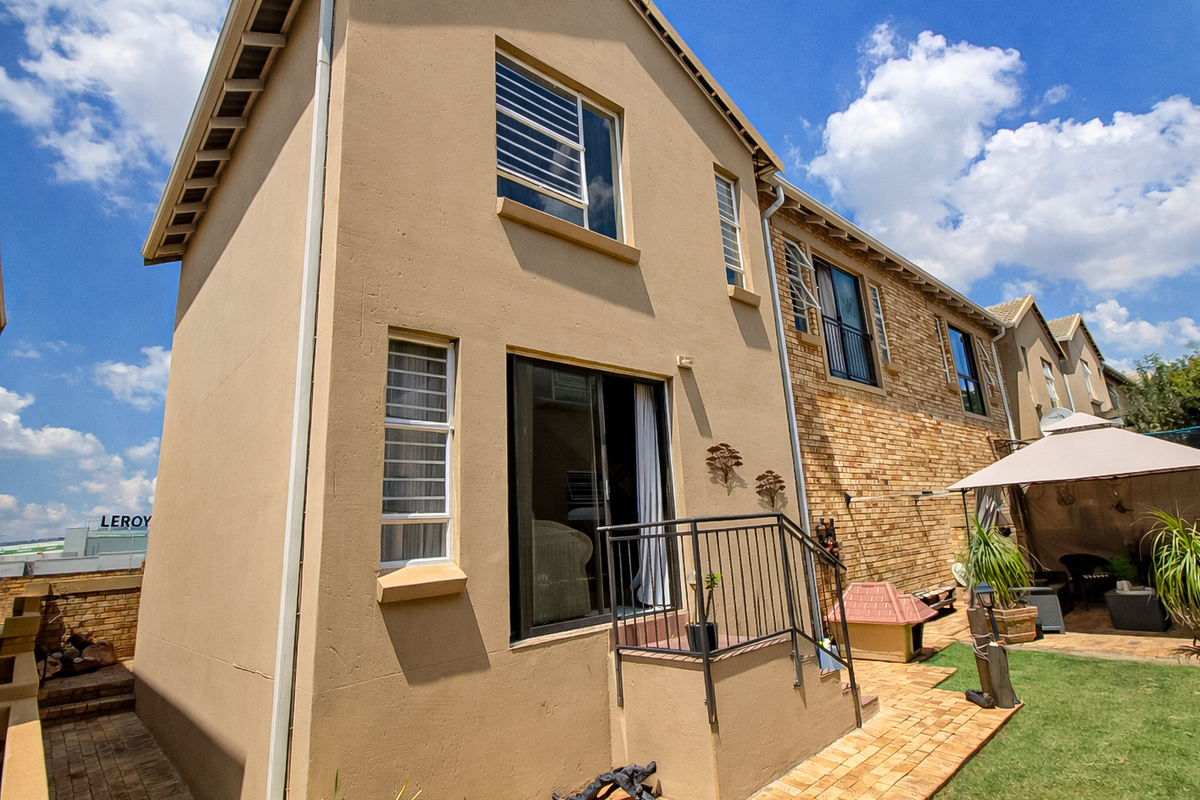 Rear view of the townhouse featuring a paved patio area, brick facade, and elevated access to the living space via sliding doors.