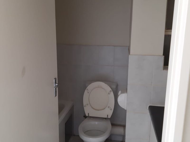 A compact bathroom featuring a standard toilet, tiled surfaces, and a vanity cabinet, presenting a functional space in need of minor cosmetic updates.