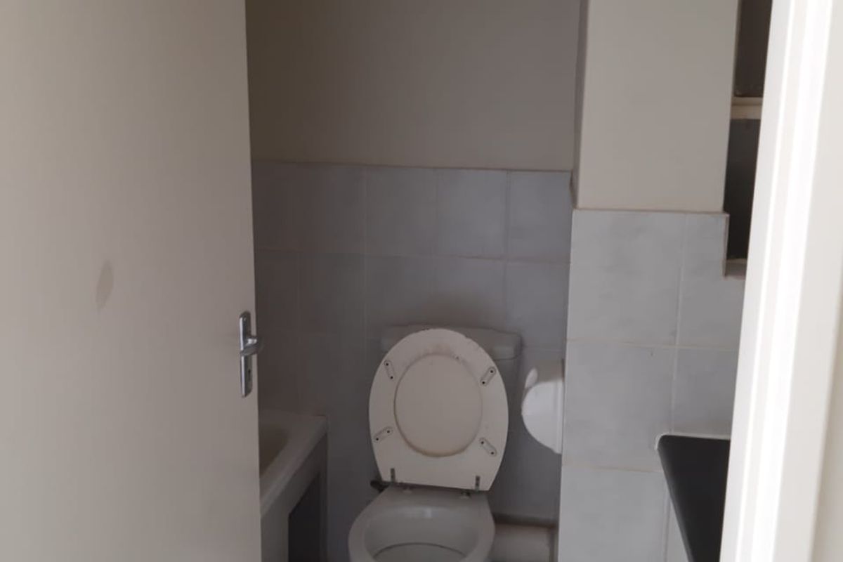 A compact bathroom featuring a standard toilet, tiled surfaces, and a vanity cabinet, presenting a functional space in need of minor cosmetic updates.