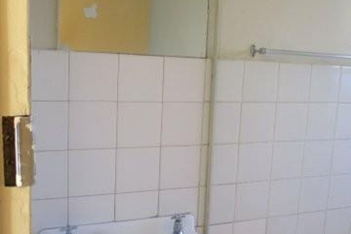 A dated bathroom featuring a wall-mounted basin, tiled splashback, and bathtub, requiring cosmetic updates and repairs to the ceiling and wall finishes.