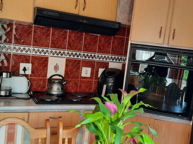 A dated kitchen featuring wood-finish cabinetry, a built-in oven, electric hob, and decorative tiled backsplash.