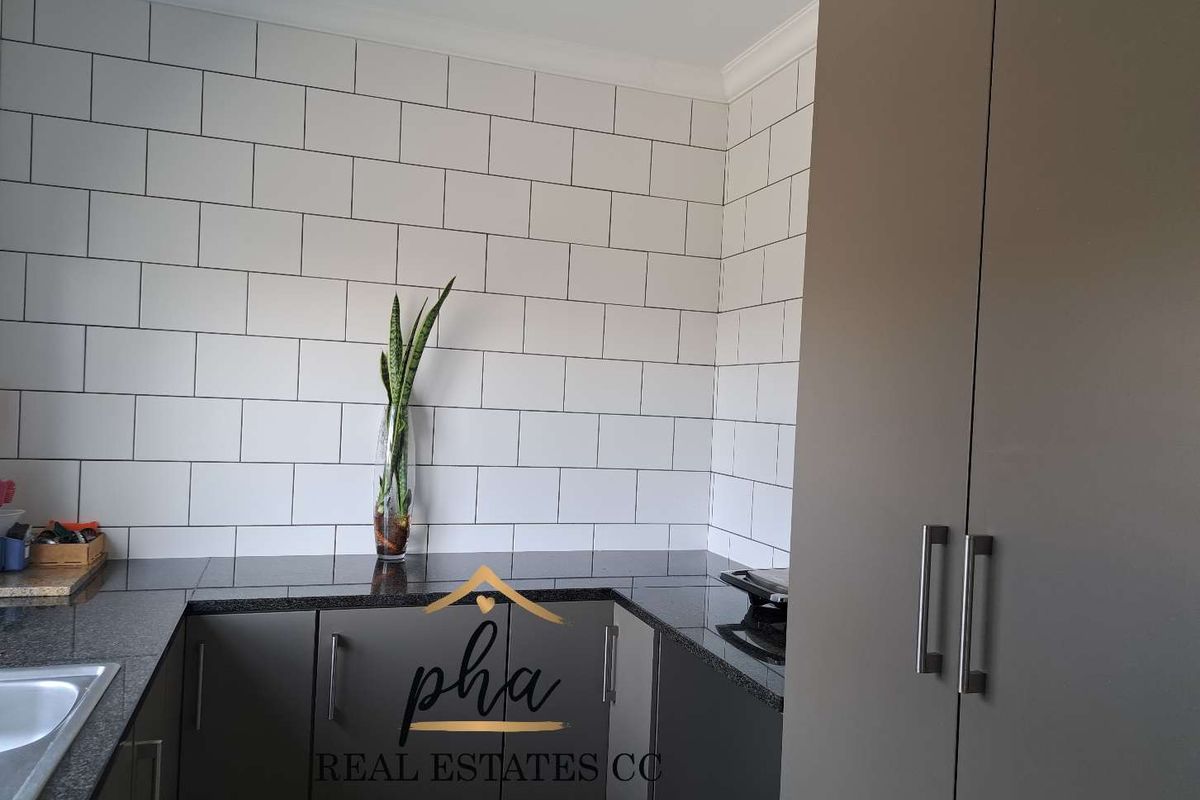 Modern kitchen area featuring sleek grey cabinetry, dark granite countertops, and a clean white subway tile backsplash.
