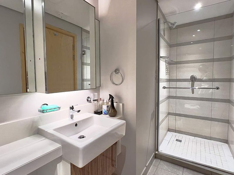 Modern bathroom featuring a vanity with basin, wall-mounted mirror, and a glass-enclosed shower with tiled finishes.
