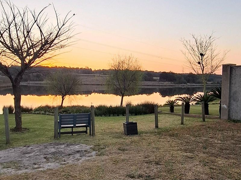 A scenic view of a tranquil lake at sunset, featuring a landscaped garden area and a solid boundary wall.