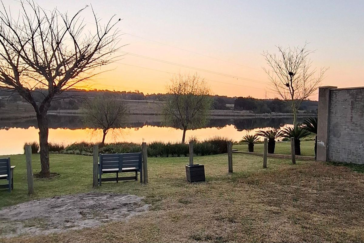 A scenic view of a tranquil lake at sunset, featuring a landscaped garden area and a solid boundary wall.