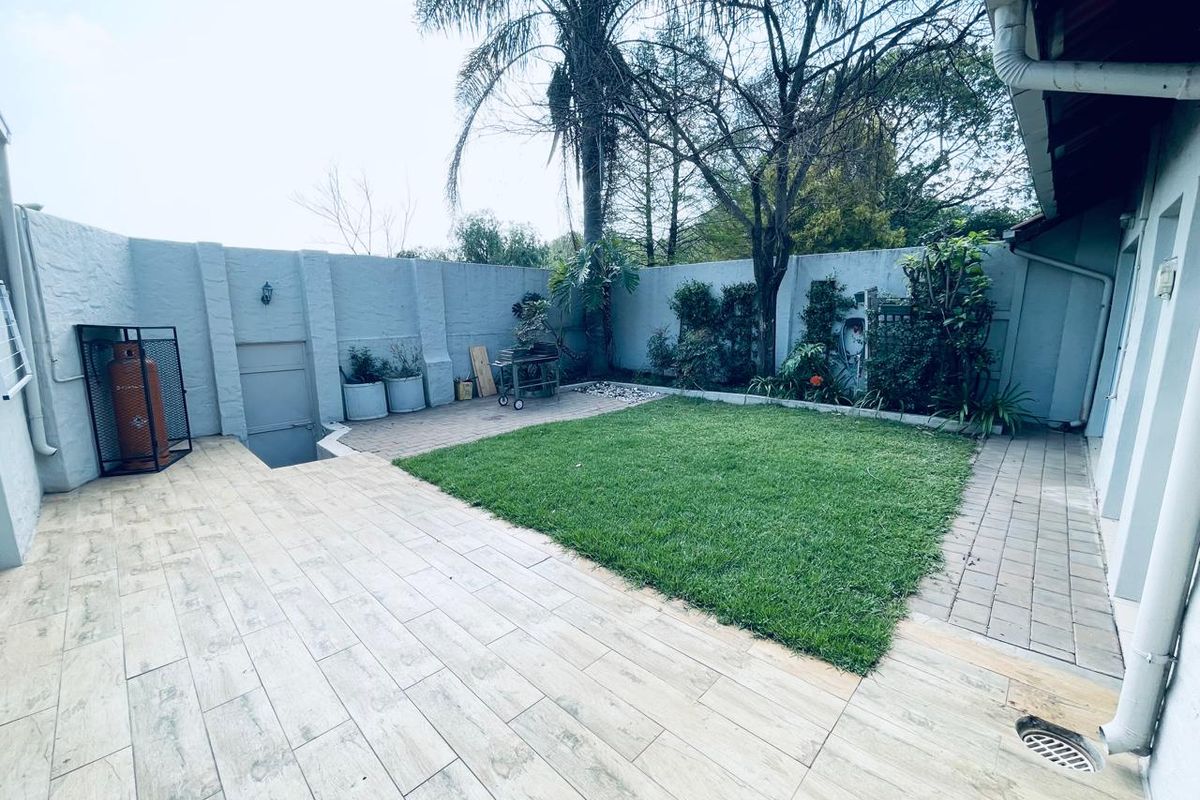 A private rear garden featuring a paved patio area, a well-maintained lawn, and high boundary walls for added privacy.
