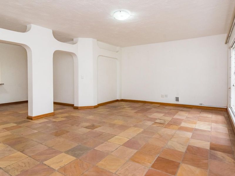 An empty, open-plan living area featuring distinctive arched architectural dividers, natural stone tile flooring, and large sliding glass doors providing ample natural light.