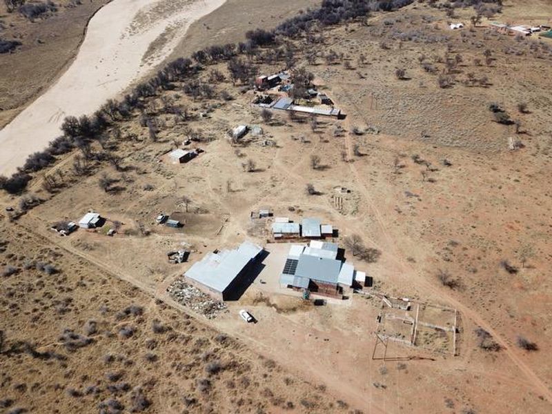 Aerial view of a rural small holding featuring multiple outbuildings, metal roof structures, solar panels, and fenced enclosures set within a large landscape.
