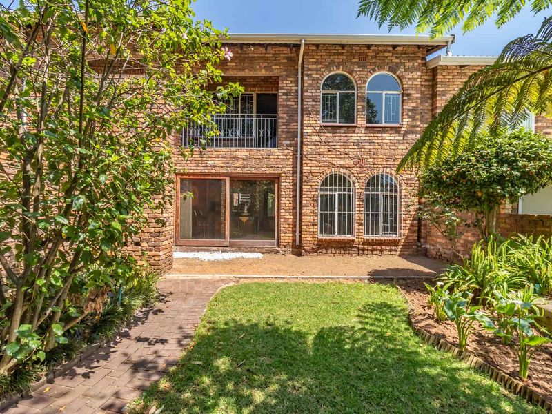 Rear view of a face brick townhouse featuring a private garden, paved walkway, arched windows, and an upper-level balcony.