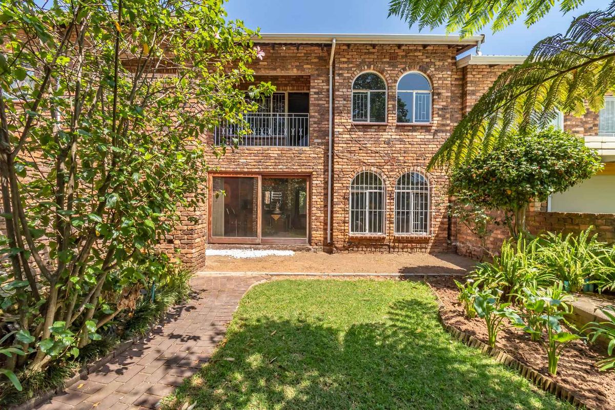 Rear view of a face brick townhouse featuring a private garden, paved walkway, arched windows, and an upper-level balcony.